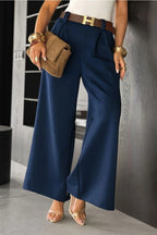 Person wearing navy blue wide-leg pants with a brown belt and clutch, standing against a neutral wall.