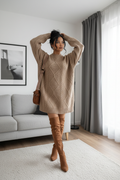 Woman in a beige sweater and brown knee-high boots standing in a living room.
