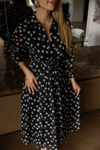 Woman wearing a black dress with white polka dots in a room.