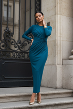 Woman in a teal dress standing on steps outside a building with decorative ironwork.