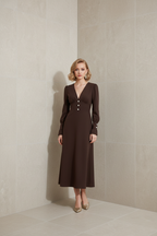 Woman wearing a brown dress standing against a beige wall.